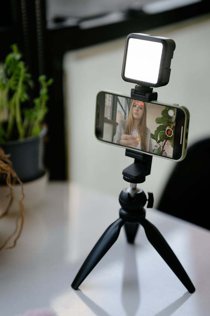 Smartphone mounted on a tripod recording a vlogger indoors with lighting.